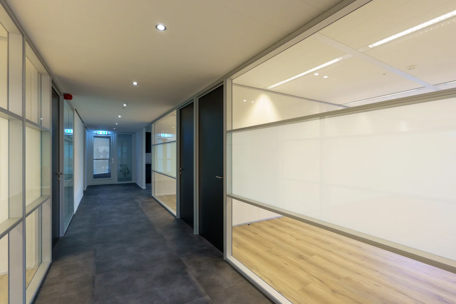 Verlichte gang in een modern kantoorpand aan de Baarnsche Dijk met glazen wanden en zicht op kantoorruimtes.